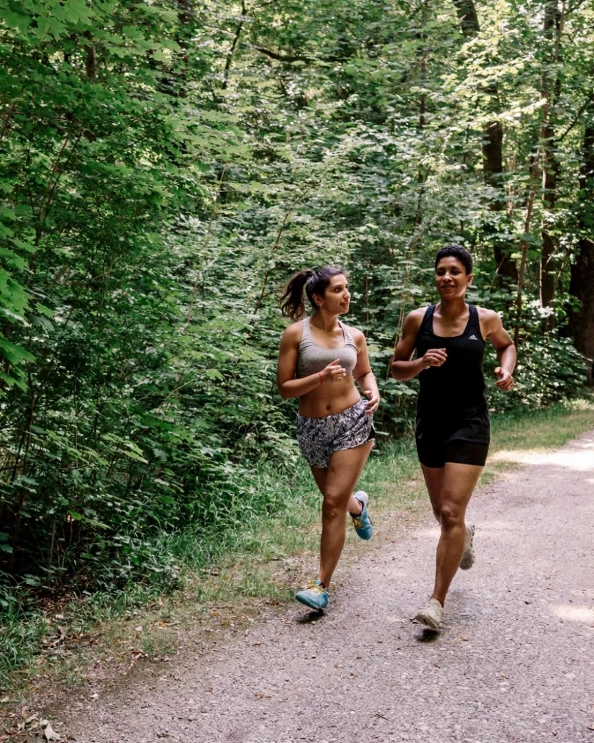 Two women running together on forest trail, showcasing natural movement and community connection in nature