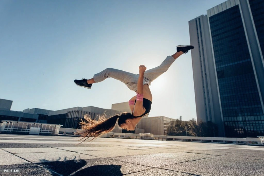 Woman performing dynamic handstand freeze move on urban rooftop with city buildings, showcasing strength, balance and athletic performance
