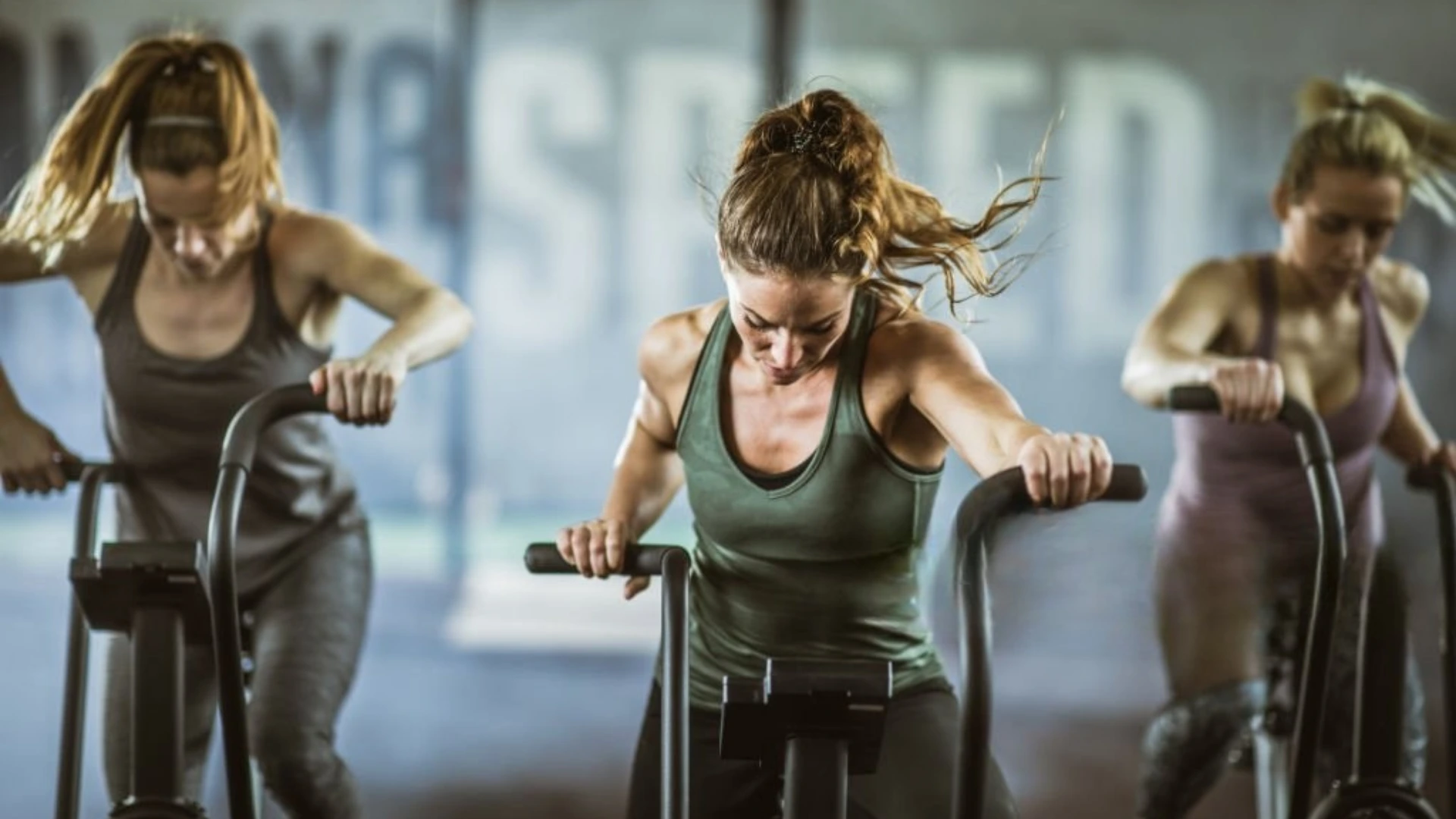 Three women doing intense cardio cycling workout in gym, showcasing group fitness and high-intensity training