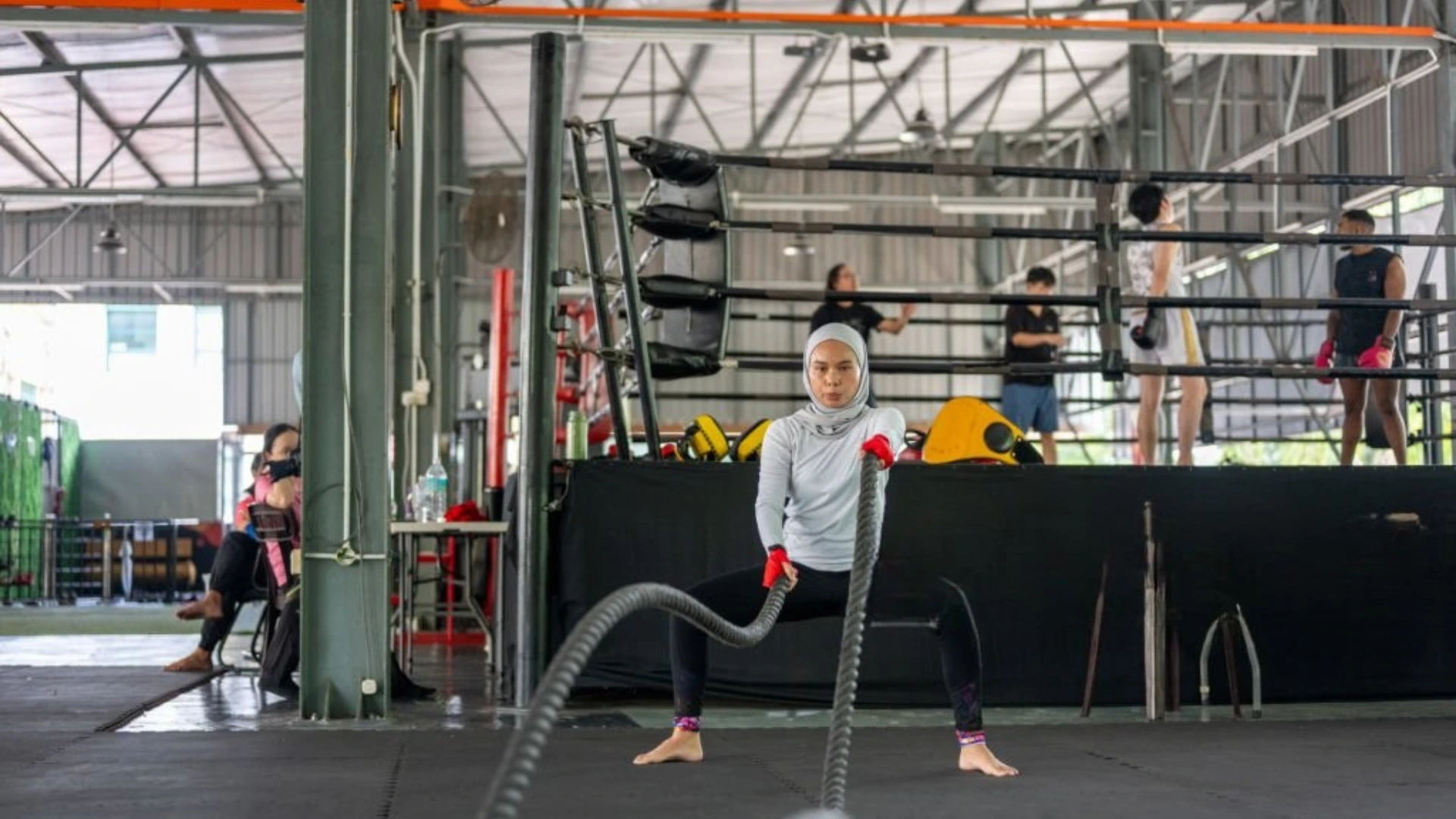 Woman doing battle rope training in industrial gym setting, showcasing high-intensity functional fitness and purposeful movement